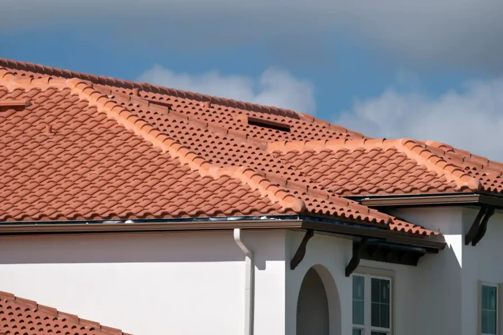 Overlapping rows of terracotta ceramic roof tiles with a blue sky and clouds.