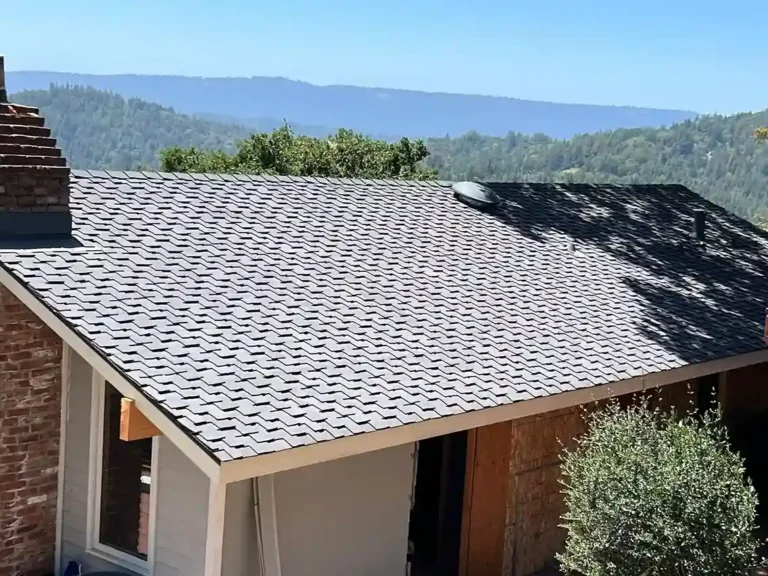 Home with newly installed asphalt shingle roof surrounded by forested mountains in the background.