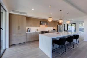 Modern kitchen remodel featuring wood cabinetry, marble island, pendant lighting, and black bar stools.