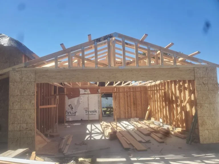 Wood-framed garage under construction with exposed beams, plywood sheathing, and Tyvek house wrap visible.