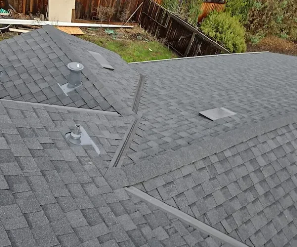 Aerial view of a newly installed composite shingle roof with ridge vents, flashing, and multiple roof lines.