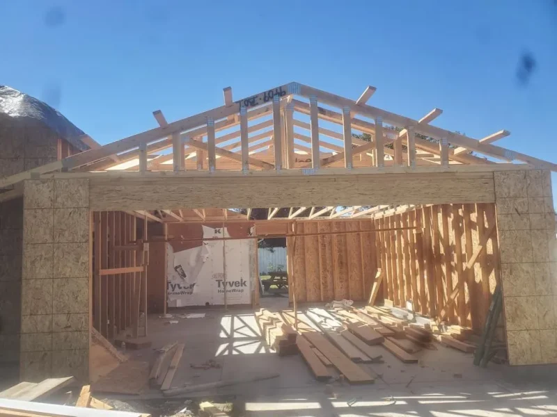 Wood-framed garage under construction with exposed beams, plywood sheathing, and Tyvek house wrap visible.